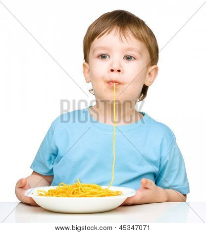 Little boy è succhiare un filamento singolo spaghetti, isolato su bianco
