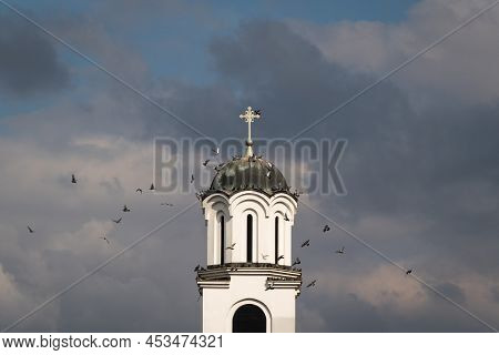 Flock Of Pigeons Fly Around Church Bell Tower Against Dark Stormy Clouds