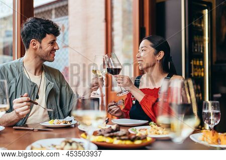 Smiling Interracial Couple Toasting With Wine In A Bar
