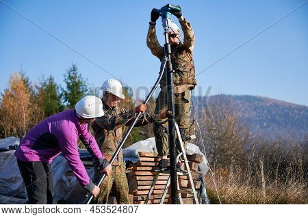 Male Workers Building Pile Foundation For Wooden Frame House. Men Builders In White Safety Helmets D
