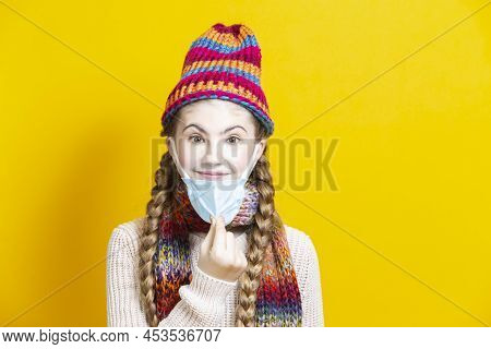 Teenage Girl In Warm Knitted Hat And Scarf Using Facial Mask Against Viruses While Posing Over Trend