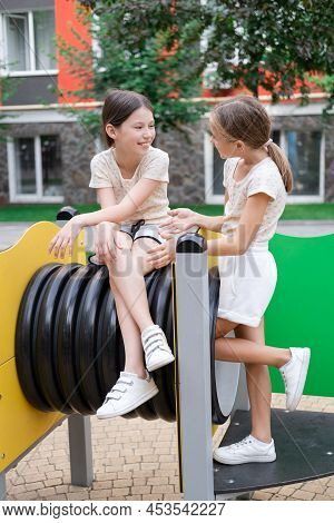 Two Pretty Teen Girls Playing On A Modern Playground In Identical Clothes. Sister, Bffs. Sisterhood,