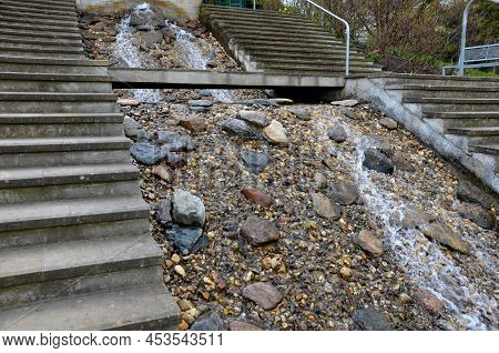 Between The Stairs Is A Waterfall With Stones And Boulders. Artificial Stream With A Waterfall Betwe