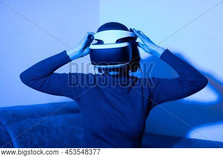 Girl Putting On A Vr Helmet To Enter The Virtual Universe At Home In Blue Light. The Concept Of The 