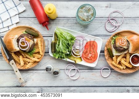 Sliders And Fries On Wooden Plates With A Platter Of Toppings In The Middle.