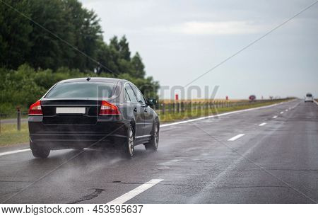 A Black Passenger Car Drives On A Wet Highway In Summer. Slippery Road. Copy Space For Text
