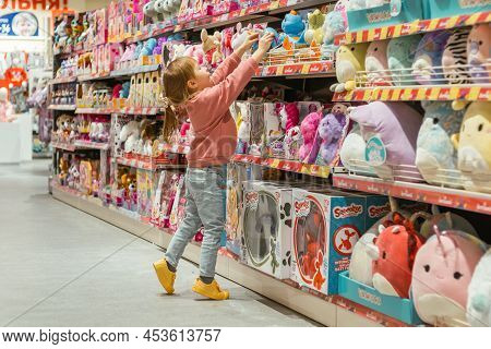 Little Caucasian Girl Coosing A New Toy In The Big Baby Store.