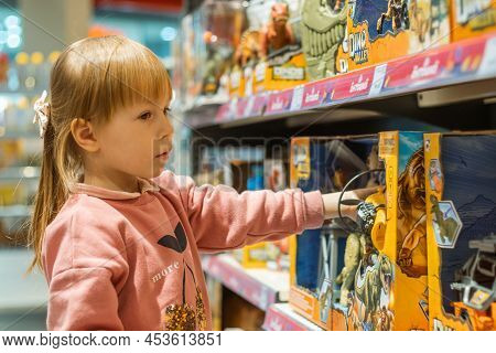 Little Caucasian Girl Coosing A New Toy In The Big Baby Store.
