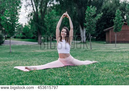 Attractive Young Caucasian Woman In Nature. Handsome Brunette Doing Yoga In Pose Monkey Pose Hanuman