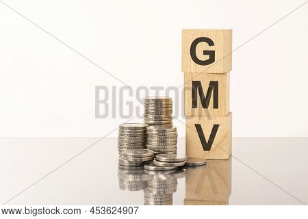 The Word Gmv Is Laid Out Of Wooden Cubes With Letters On White Background With Coins. Gmv - Short Fo