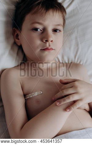 Sad Sick Boy With Thermometer Lying In Bed