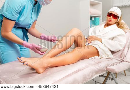Depilation And Epilation. Professional Cosmetologist In Pink Medical Gloves Spread Agent Gel To The 