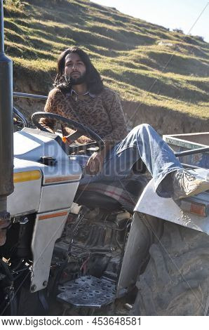 An Indian Bearded And Long Haired Young Male Model Posing With Sitting On An Old Tractor In The Moun