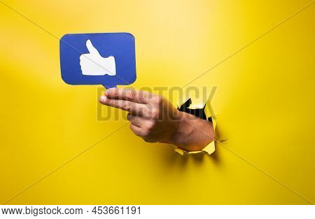 Hand Holding Social Approval Sign, Like, Thumbs Up Through Torn Yellow Wall