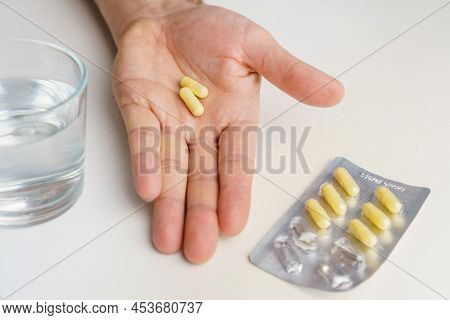 Close-up Hand Holding Medicine Capsule And Glass Of Water Pills In Blister At Background. Man Taking