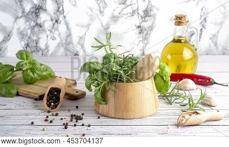 Basil And Rosemary In Wooden Mortar With Oil , Peppper And Salt On A Wooden Spoon