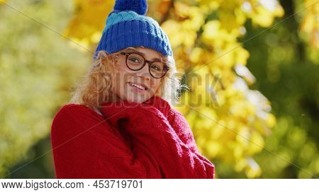 Outdoor Autumn Portrait Of A Cosily Dressed Caucasian Blond Girl Looking At Camera And Smiling. Warm