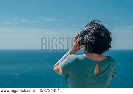 Portrait Adult Woman Listens To Music In Headphones In Summer, Spring Against The Backdrop Of Mounta