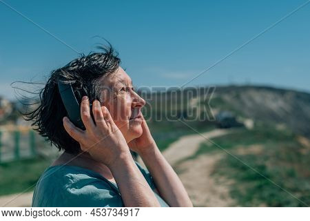 Portrait Adult Woman Listens To Music In Headphones In Summer, Spring Against The Backdrop Of Mounta