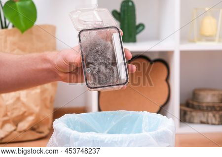 A Man Shakes Out A Garbage Container From A Robot Vacuum Cleaner. The Container Is Full Of Wool, Dus