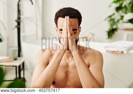 Young Shirtless Man Holding His Hands In Front Of His Face And Meditating With His Eyes Closed In Th