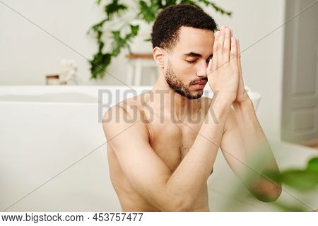 Young Shirtless Man Concentrating During Meditation While Sitting In Bathroom