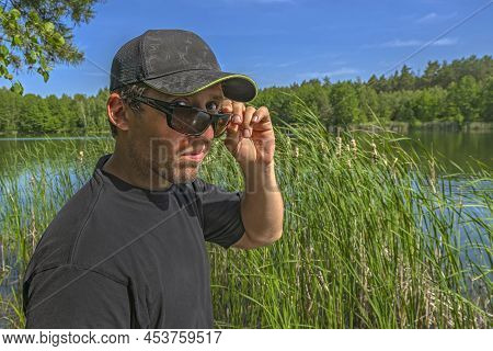 Skeptical Look. Man In Cap Watches From Under Sunglasses With Contempt, Doubtful And Scepticism Outd