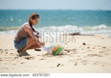 Young Female Coastkeeper Picking Up Ocean Trash On Beach