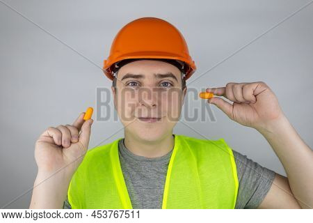 A Worker In A Hard Hat And Green Vest Puts On Ear Plugs. Industrial Safety. Industrial Noise Protect