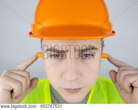 A Worker In A Hard Hat And Green Vest Puts On Ear Plugs. Industrial Safety. Industrial Noise Protect