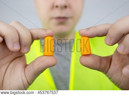 A Worker In A Hard Hat And Green Vest Puts On Ear Plugs. Industrial Safety. Industrial Noise Protect