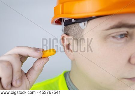 A Worker In A Hard Hat And Green Vest Puts On Ear Plugs. Industrial Safety. Industrial Noise Protect