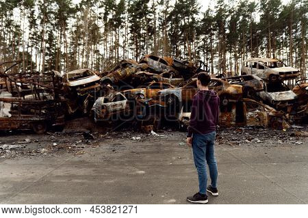 Ukrainian Man Stands Against The Background Of Broken And Burnt Cars Affected By Russian Missiles. D