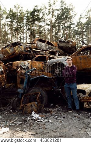 Ukrainian Man Stands Against The Background Of Broken And Burnt Cars Affected By Russian Missiles. D