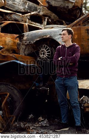 Ukrainian Man Stands Against The Background Of Broken And Burnt Cars Affected By Russian Missiles. D