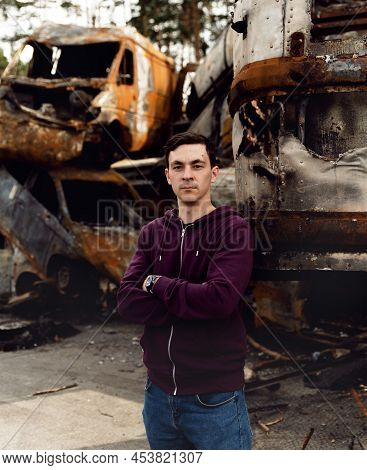 Ukrainian Man Stands Against The Background Of Broken And Burnt Cars Affected By Russian Missiles. D