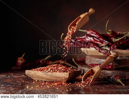 Chilli Flakes Are Poured Into A Wooden Dish. Chilli Flakes And Dried Chili Peppers On A Brown Backgr