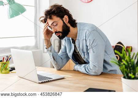 Exhausted Young Businessman Having Headache While Working In Home Office. Overworked Freelance Man W