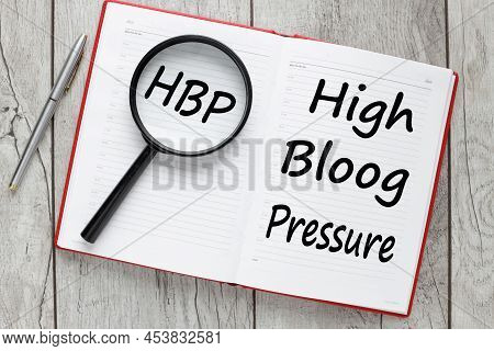 Hbp High Blood Pressure Text On A Glass Of A Magnifying Glass On An Open Notepad On A Working Table