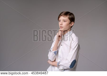 Thoughtful Young Teen Man Holding Hand On Chin Indecision Pose In White Shirtisolated On Gray Studio