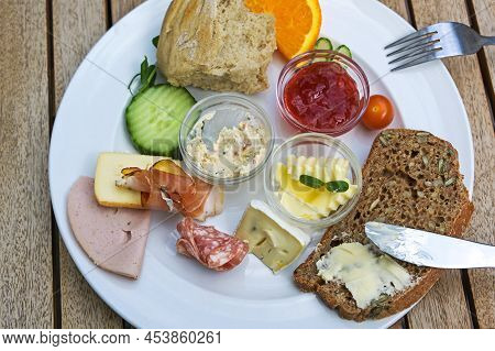 Breakfast Or Lunch Plate With Various Cold Cuts, Whole Meal Bred, Jam And Fruits On A Wooden Table I