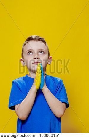 Ukrainian Boy Prays For Ukraine. Children Against War. A Boy In A Blue T-shirt On A Yellow Backgroun