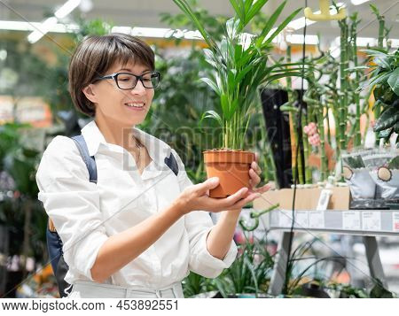 Woman Chooses Plants For Home. Shelves With Seedlings, Flowering Plants And Seeds In Flower Shop. In