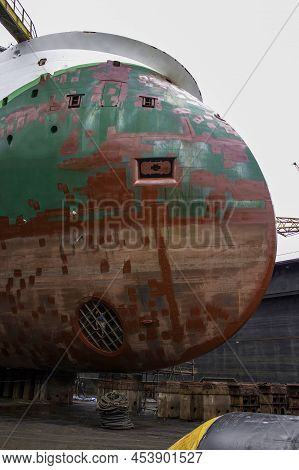 Ship High And Dry On Blocks In Drydock. Worker Inspecting Bow Thruster. Hull Spot Painted With Red P
