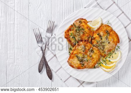 Parmesan Breaded Seared Chicken Breasts With Lemon Butter Caper Sauce On White Plate On White Wooden