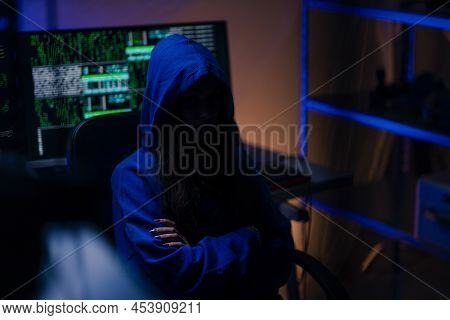 Hooded Anonymous Hacker By Computer In The Dark Room At Night, Cyberwar Concept.