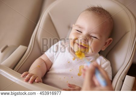 Mother Feeding Her Cheerful Baby Boy Using Spoon, Introducing First Solid Food Meal, Baby Sitting In