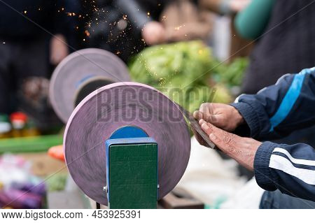 Man Holding In Hands Axe Closeup And Using Sharpening Machine. Senior Man Hands Sharpening Rusty Axe