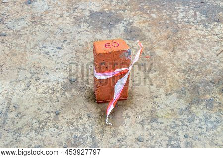 A Brick With A Red Inscription 60 Is Tied With A Signal Tape And Stands In A Puddle Of Water On A Co