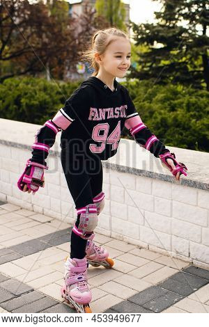 Girl Child Rollerblading In Fall Protection In The Park. A Happy Child Actively Spends His Free Time